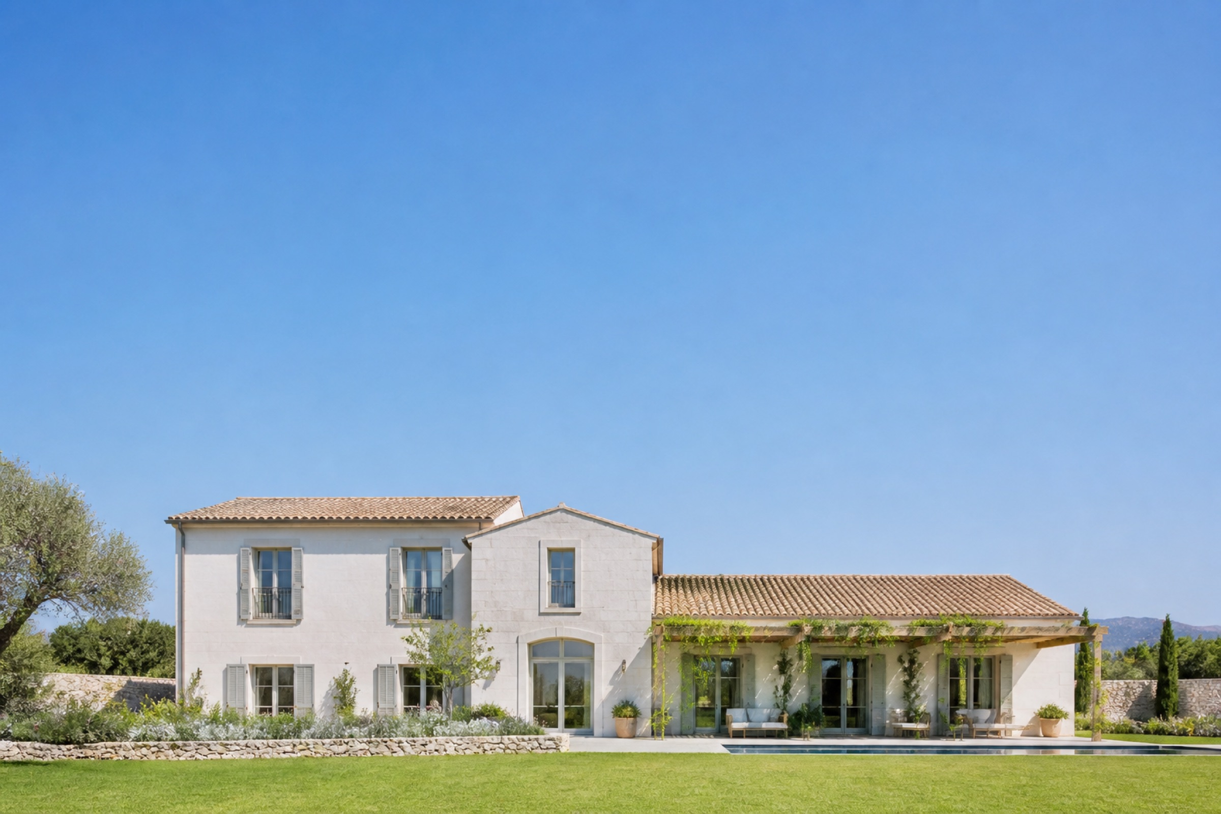 A sunlit villa with a lawn and pool under a clear sky.